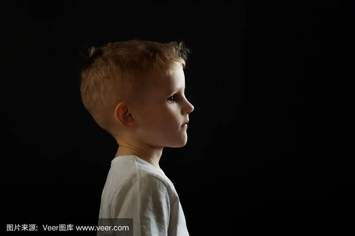 在黑色背景上的一个孩子的侧面肖像.男孩向前看,概念