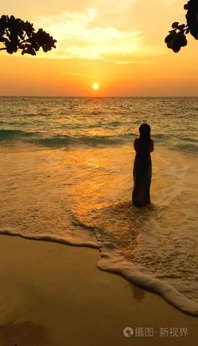 一个女人站在海边在美丽的夕阳中的剪影