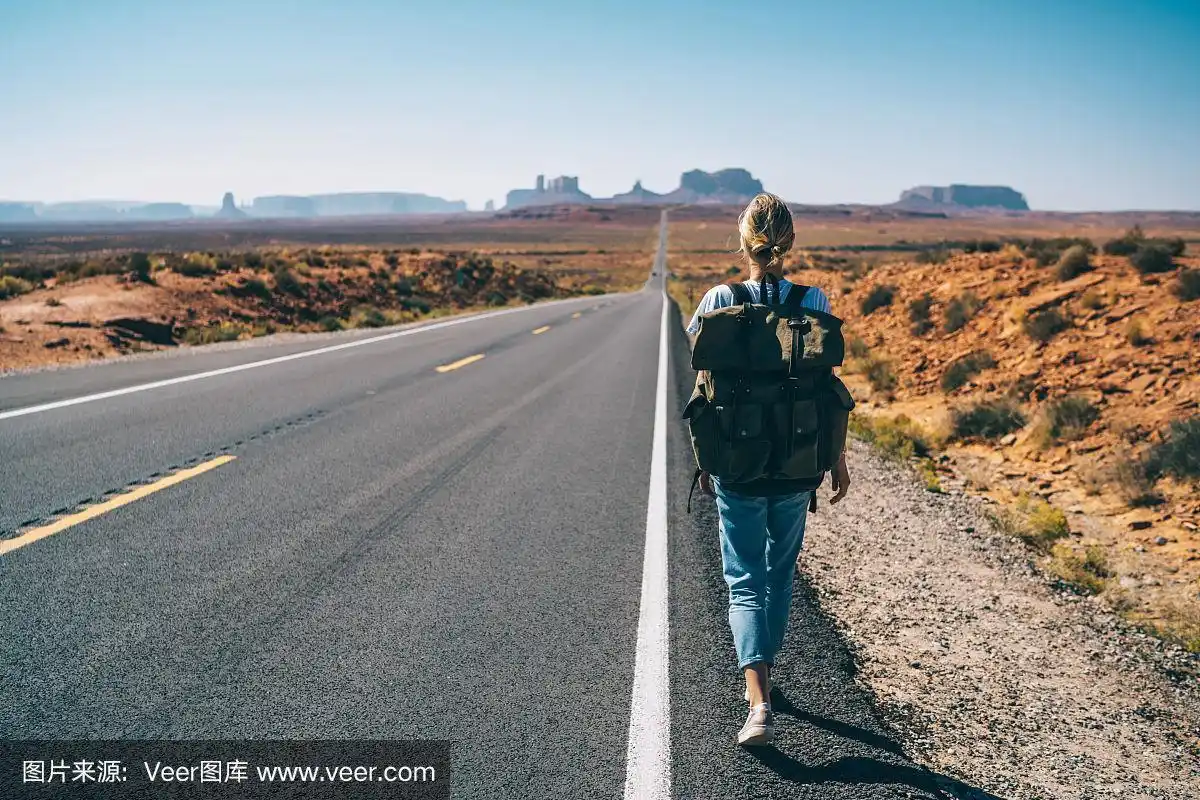 嬉皮女孩的背影漫步在柏油路在荒野西南步行到国家公园