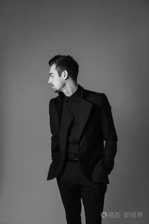 黑白肖像一个年轻英俊的男人穿着西装,站着,双手插在口袋里,看着一边