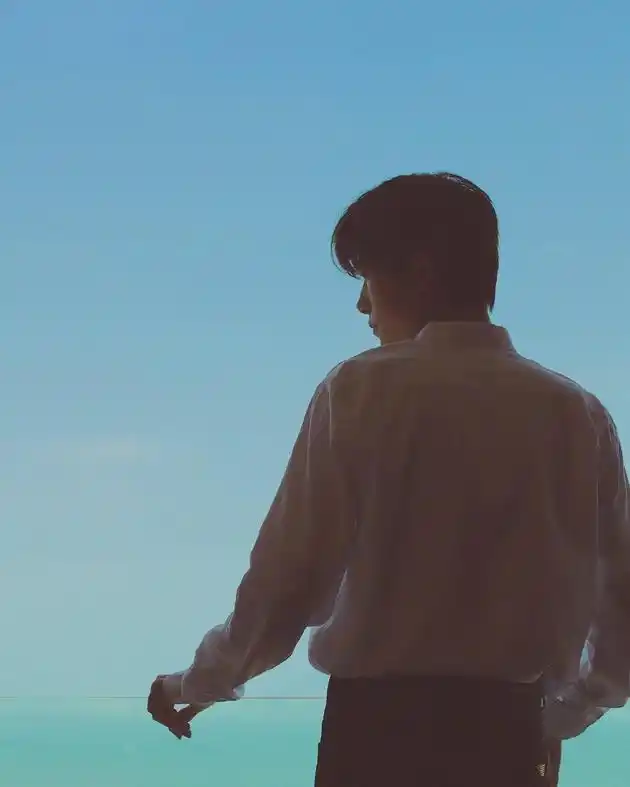 照片中,易烊千玺身穿白色衬衣,手倚在玻璃围栏上,背影帅气依旧,低眉