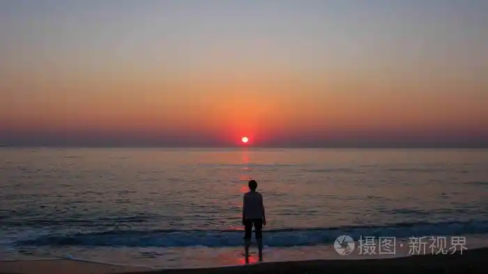 晴朗的蓝天大海太阳和黎明时分海边一个人的轮廓