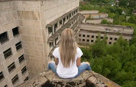 金发女郎正坐在废墟的房子在白色的 t 恤,背对相机的屋顶的边缘上照片