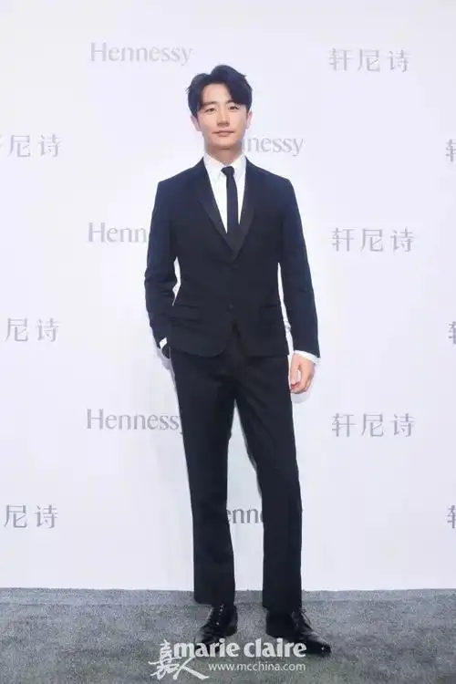 黄轩身穿黑色缎面翻领西装,戴绸缎领带,内搭白衬衣,下身穿直版西裤