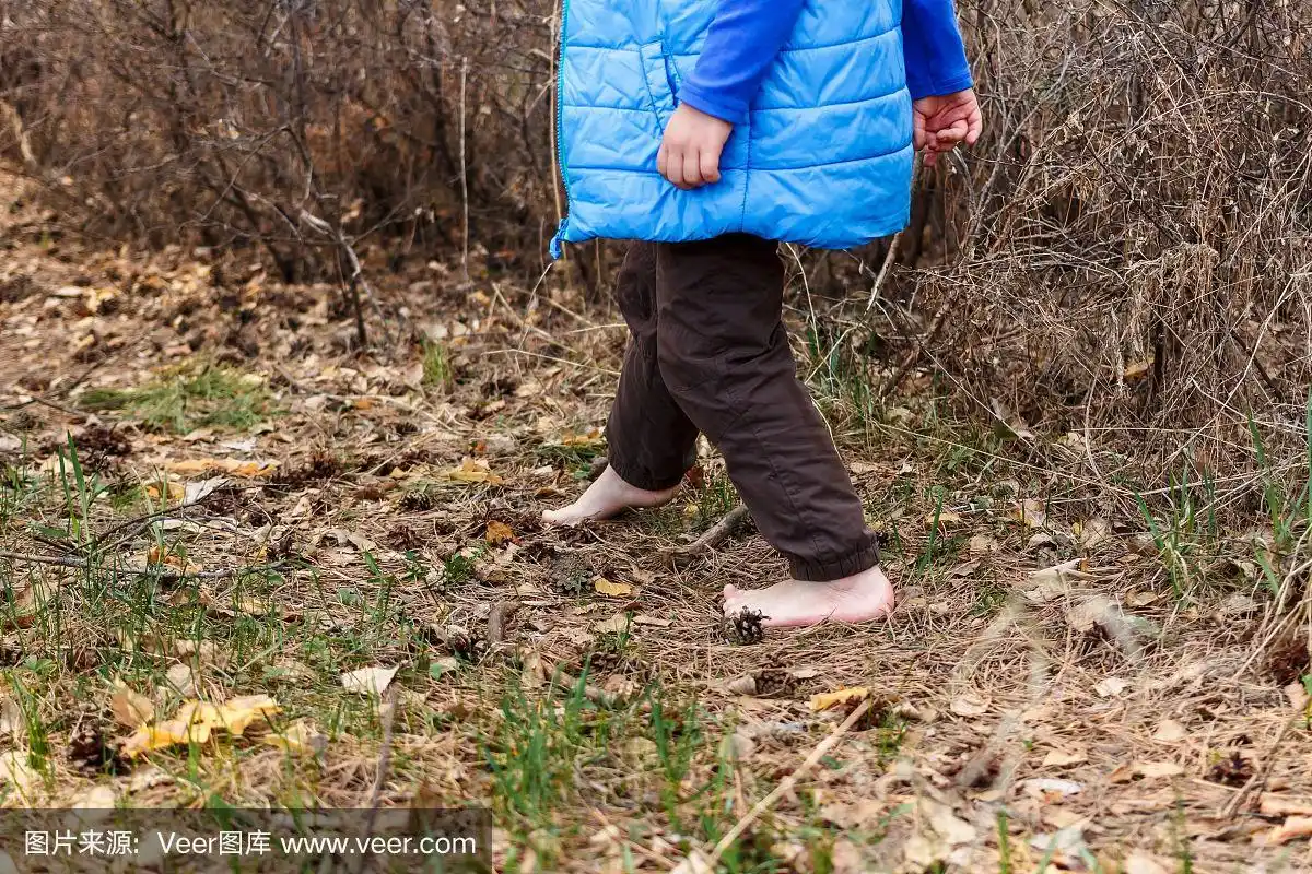 一个小孩赤脚在森林里的干草和树叶上行走