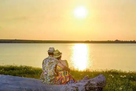 那个和那个女孩在一起的人坐在湖岸上. 日落在水的背景上.