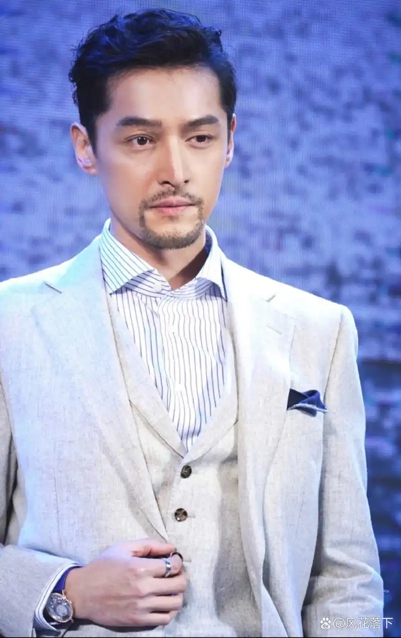 胡歌穿着白色西装和灰色马甲,黑色衬衣,系着领带,手戴着一块手表,皮肤