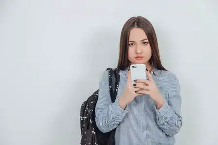 可爱的亚洲学生女孩拿着手机好像在拍照,摆姿势.背负在她的肩上.