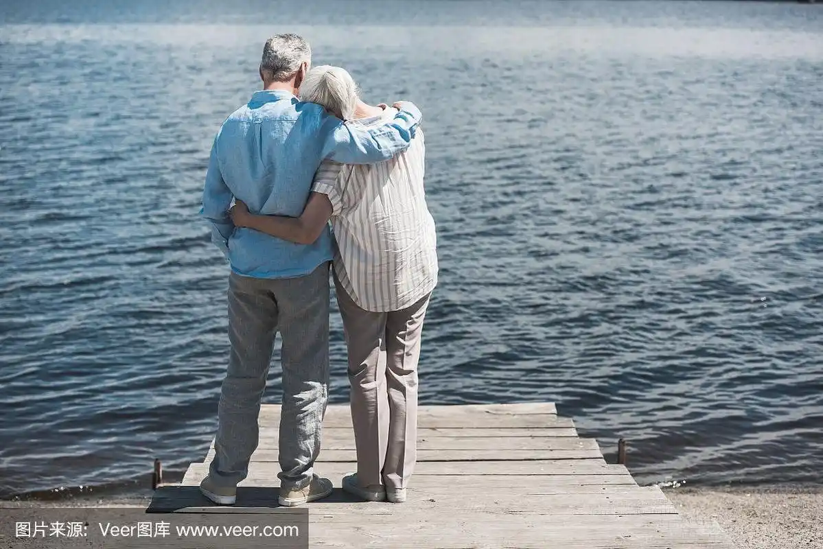 老夫妇在白天站在河边拥抱的背影