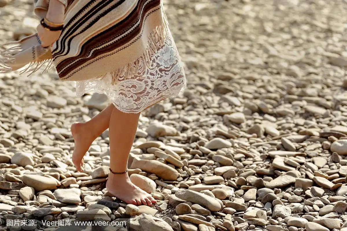 美丽的女人旅行者赤脚走在河边的海滩上,双腿收起来,波西米亚旅行的