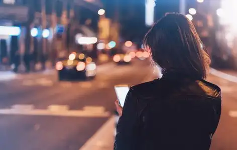 女孩指着屏幕上的智能手机背景照明发光散灯在夜间大气城市, 时髦的