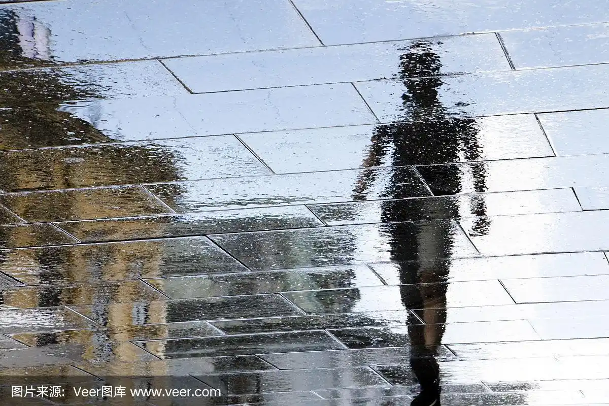 一个人走在潮湿的城市街道上,模糊的倒影剪影