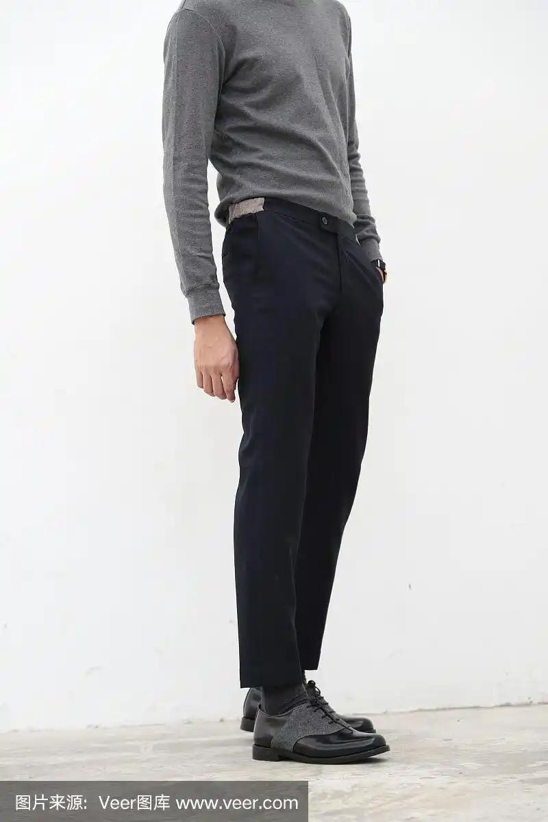 一个英俊的男人在灰色高领衬衫和黑色长裤在白色背景.