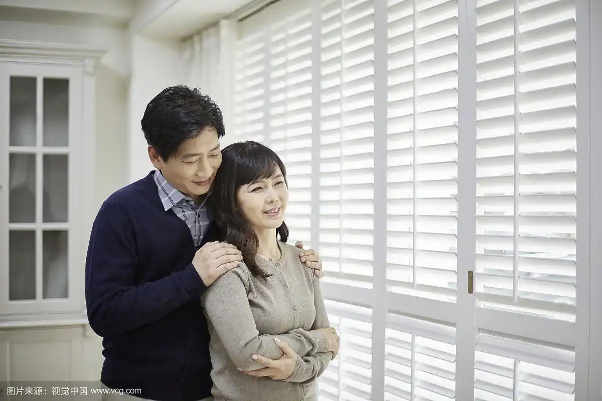 丈夫拥抱站在窗边的妻子的照片