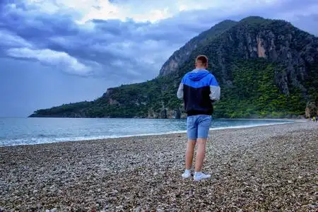带着旅游背包的年轻人, 带着石头海滩和蓝天, 在海边看着壮观的山景.