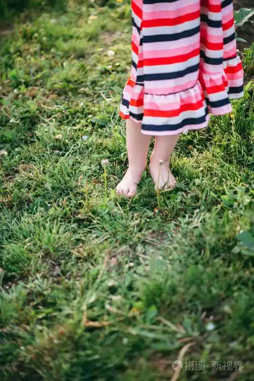 赤脚女孩在衣服上站在草地上特写