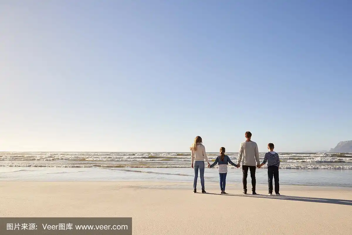 后视图的家庭在冬季海滩手牵手看海