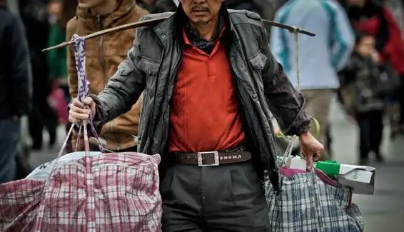 一位乘客用扁担挑着两袋行李急忙前往赶车.