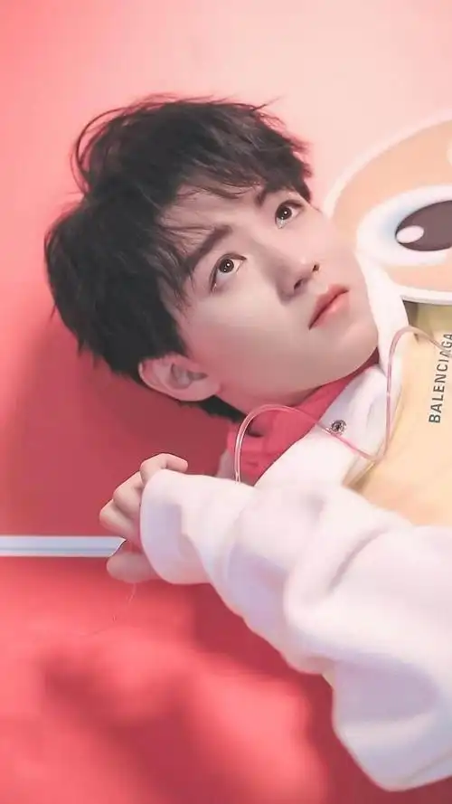 的照片,王俊凯躺在红色背景的地方,手自然地放到耳边,表情无辜又呆萌