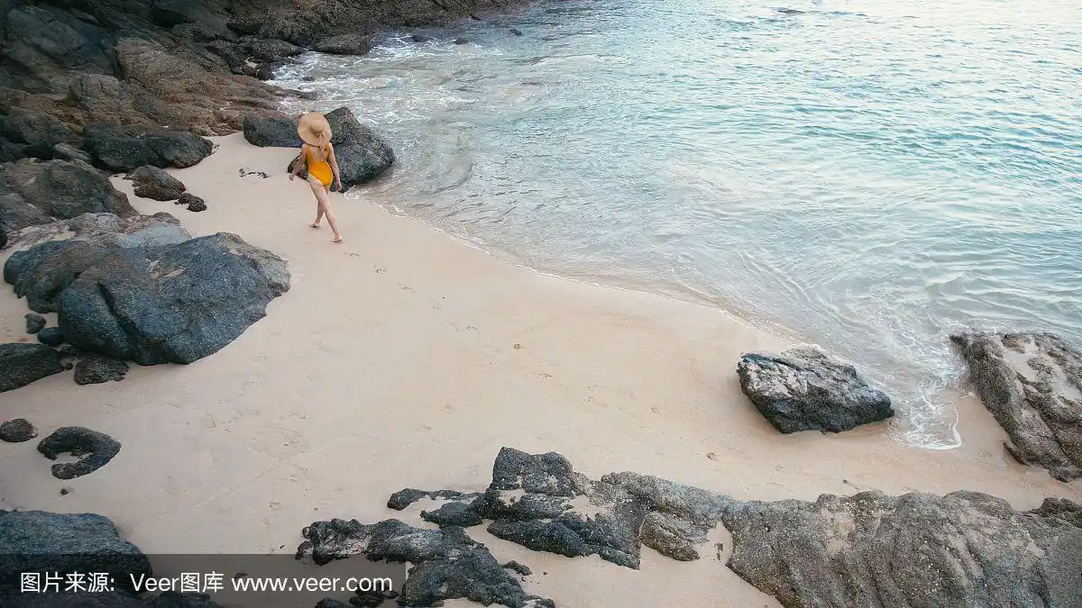 背影年轻女子在黄色泳衣走在美丽的热带白色沙滩上.