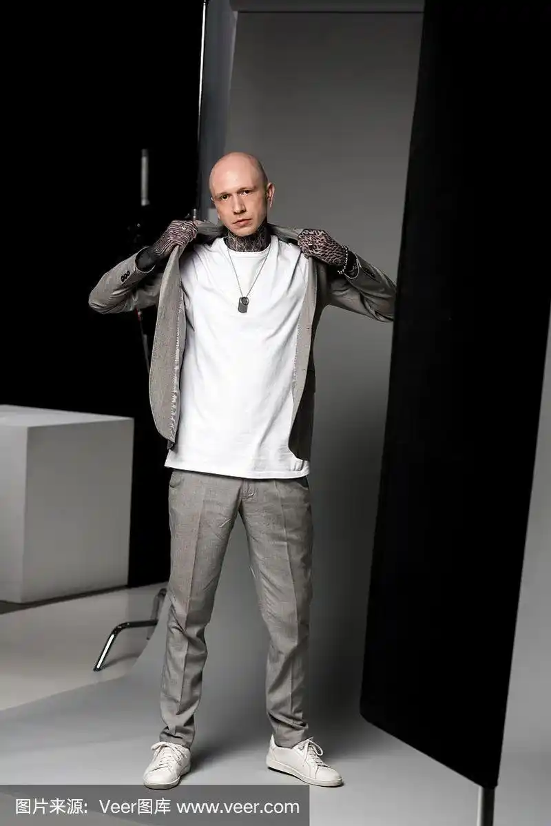 有型的光头纹身男子穿着西装夹克,在演播室看着摄像机