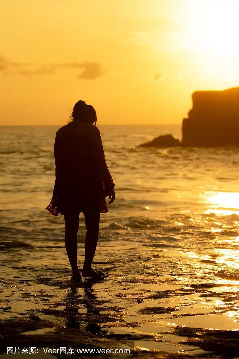 亚洲女人站在海边的海滩在日落