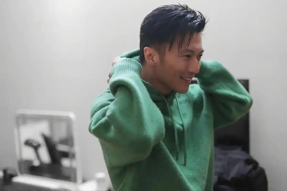 谢霆锋留着标志性的短发,身穿绿色卫衣,搭配黑色工装皮裤,专心致志