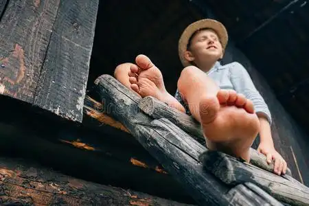那英脚赤脚男孩坐在谷仓的梯子上照片