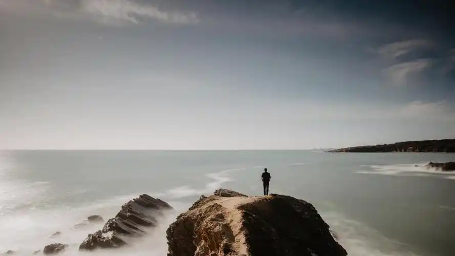 户外休闲旅游度假一人站在岩石上面朝大海背景图片