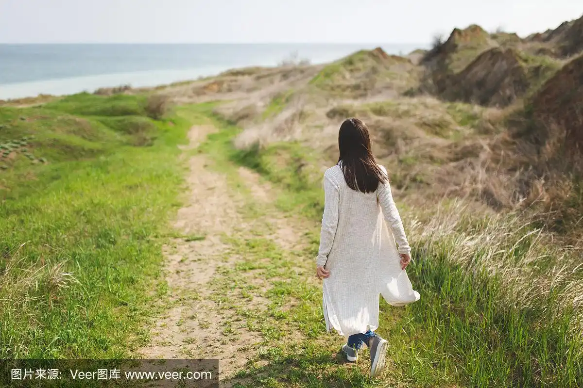 在阳光明媚的天气里,年轻的褐发女人在绿色的背景下沿着小路散步.