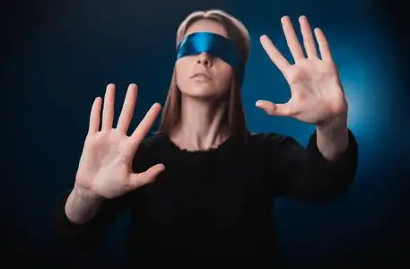 女孩蒙着眼睛,带着蓝丝带,用手找东西,在蓝色背景上玩耍,娱乐照片