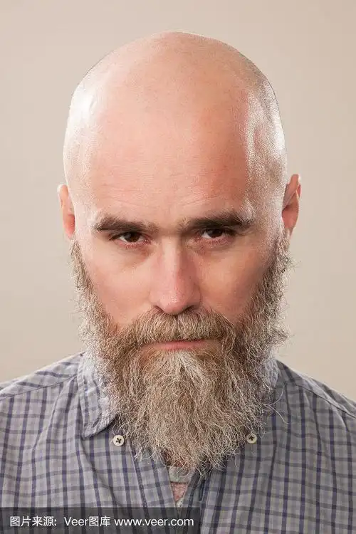 一名40岁剃着光头的大胡子男子的工作室肖像,他穿着一件米色背景的