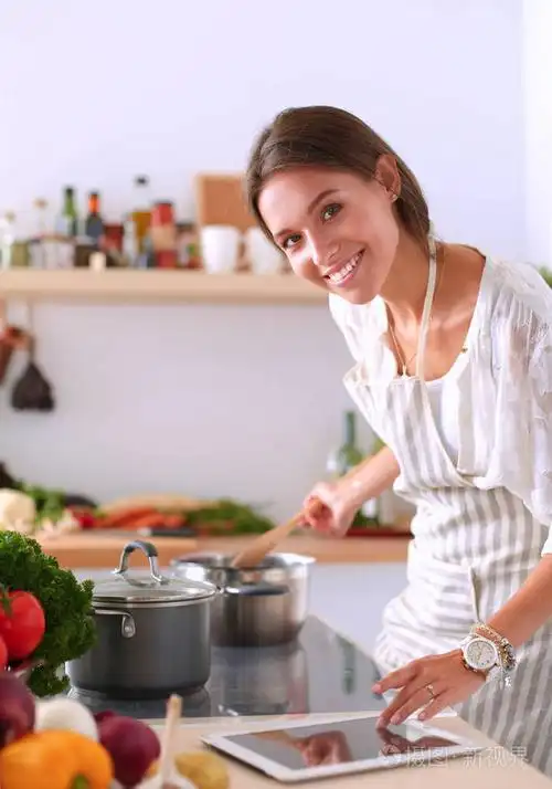 使用一台平板电脑,在她的厨房里做饭的年轻女人