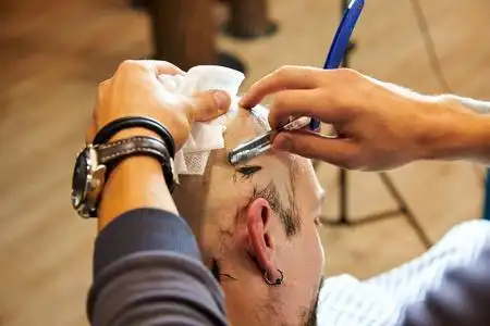 在理发店用直边剃须刀在理发店用木制纹理剃光的年轻秃头男子的肖像