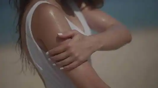 美丽的女孩子穿着泳装,在夏日的沙滩上涂抹防晒油,晒黑油,在海和天空