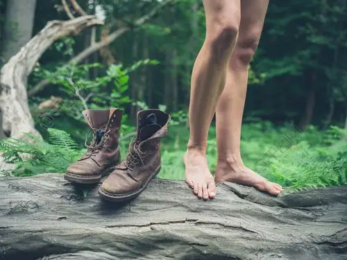 一个年轻的女人,赤脚站在一棵倒下的树在森林里与她的靴子在她旁边