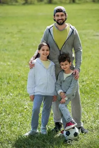 微笑的父亲抱着女儿和儿子在公园里踢球