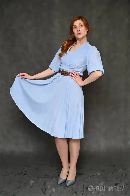 一位年轻漂亮的红发女子的全身垂直肖像,灰色背景,蓝色连衣裙.