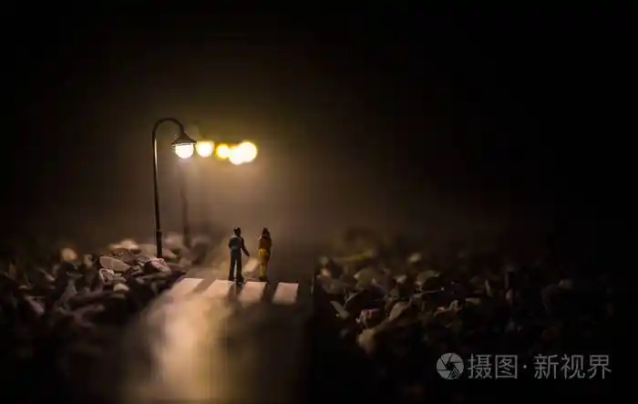 一对年轻夫妇手牵着手夜晚在白色的路灯下慢慢地走着黑暗时期雾中宁静