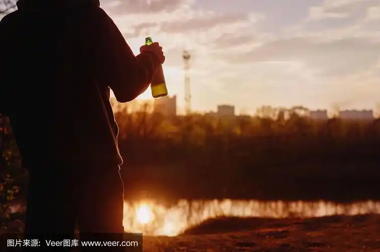 夕阳下,一个拿着啤酒瓶的男人的剪影.春季或夏季的户外休闲活动