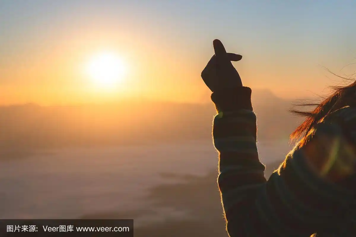 女人举起手,做了一个小心形的象征伸向太阳.复制空间,暖色调复古.