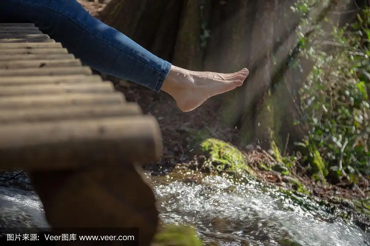 一个穿着牛仔裤的女人赤着脚坐在急流上的木凳上