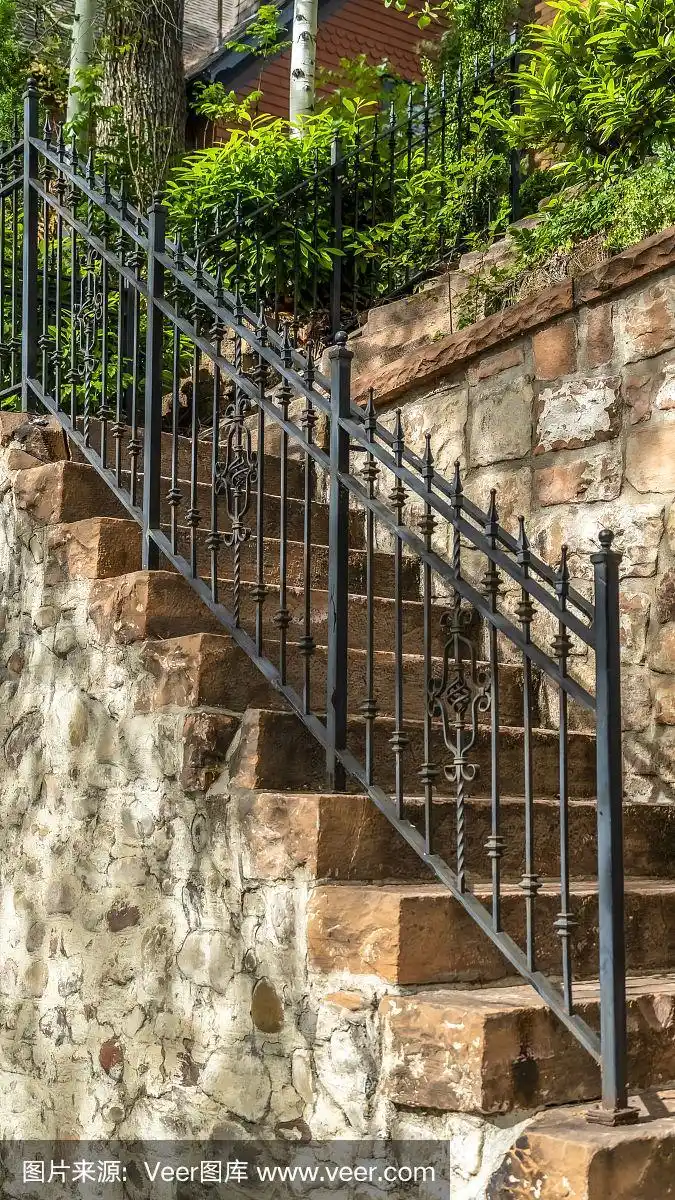 垂直室外楼梯,石阶和黑色金属栏杆对着栅栏