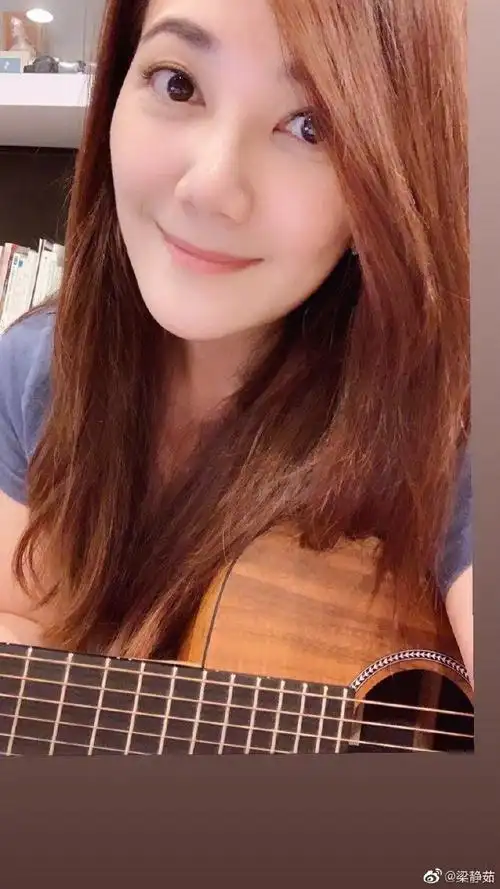 照片中的梁静茹留着披肩长发,身穿休闲短袖上衣,她抱着吉他对镜微笑