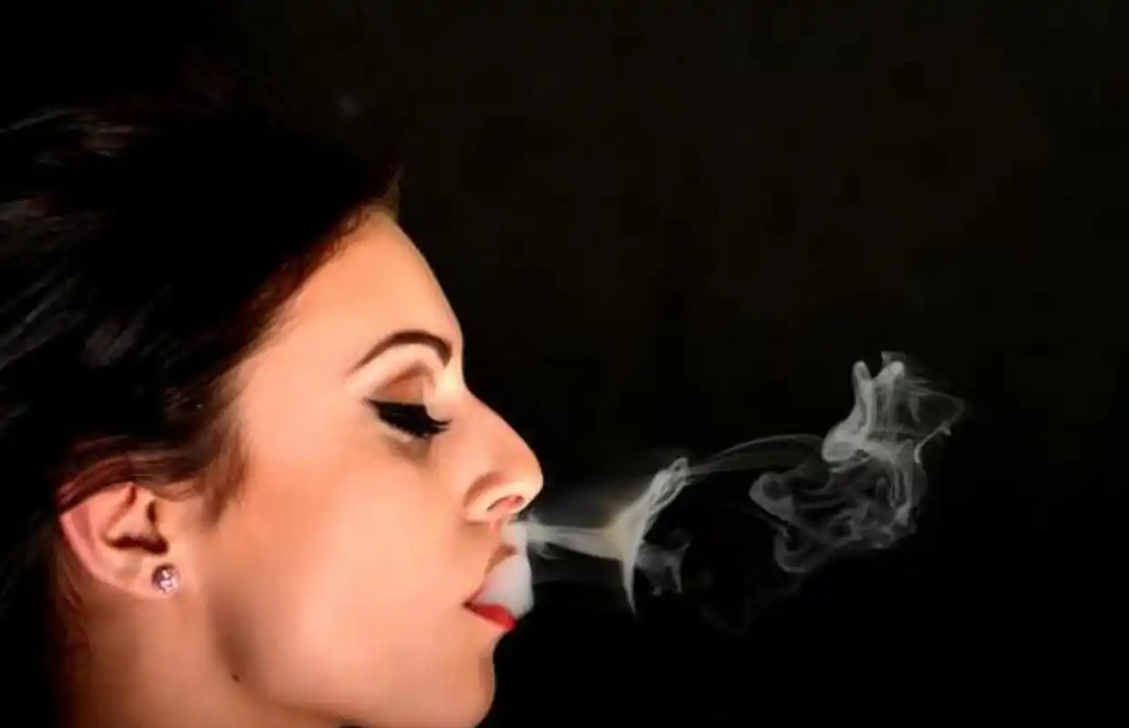 一位蹲坐在美国纽约街头的女子手里拿着香烟,正在优雅地吞云吐雾,烟雾