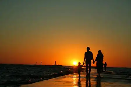 一家人在夕阳下和儿子沿着海滩散步,背影剪影海上一个家庭的轮廓.