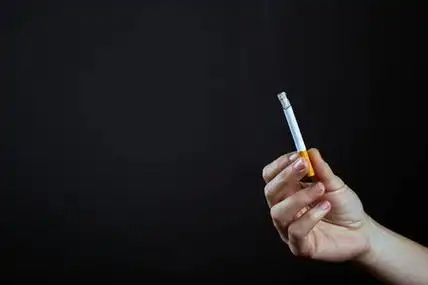 烟草危害手拿着一支点燃的香烟,背景是黑色的.尼古丁和烟草的危害照片