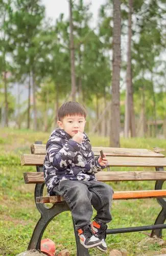 帅气十足的小男孩坐在公园长椅上吃东西
