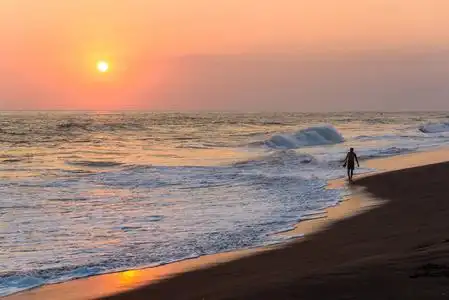 男性冲浪者在海滩上漫步日落的剪影照片