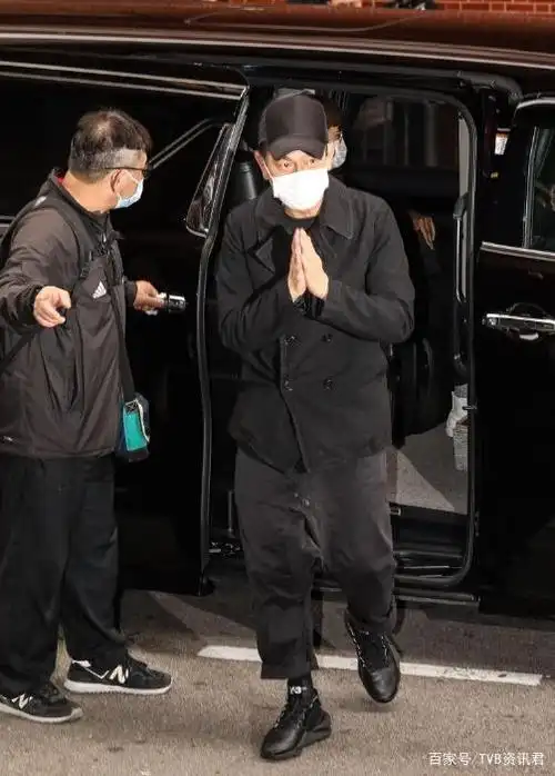 刘德华一下车便双手合十向在场的记者打招呼,他戴着cap帽和口罩,全黑